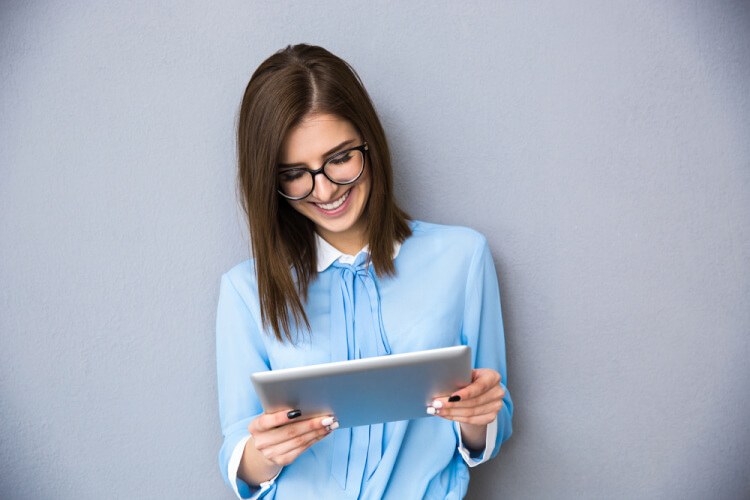 Happy businesswoman standing with table computer over gray background. Wearing in blue shirt and glasses.-1